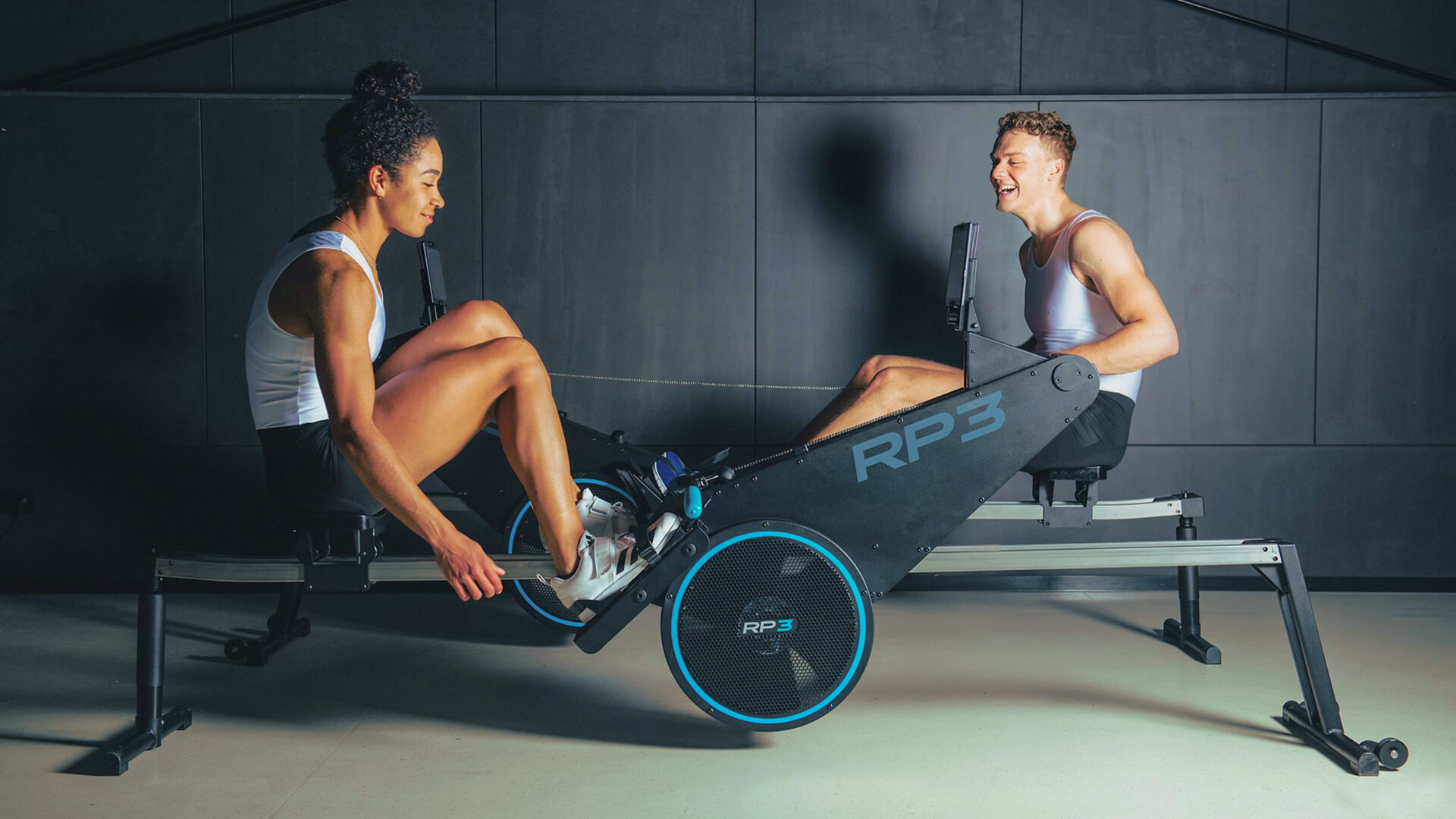 A woman and a man rowing on two RP3 Model S dynamic rowers.