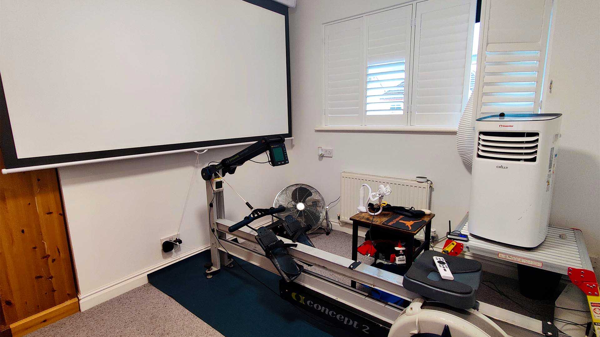 A home gym setup consisting of a fan, an air conditioner, rowing machine and projector.