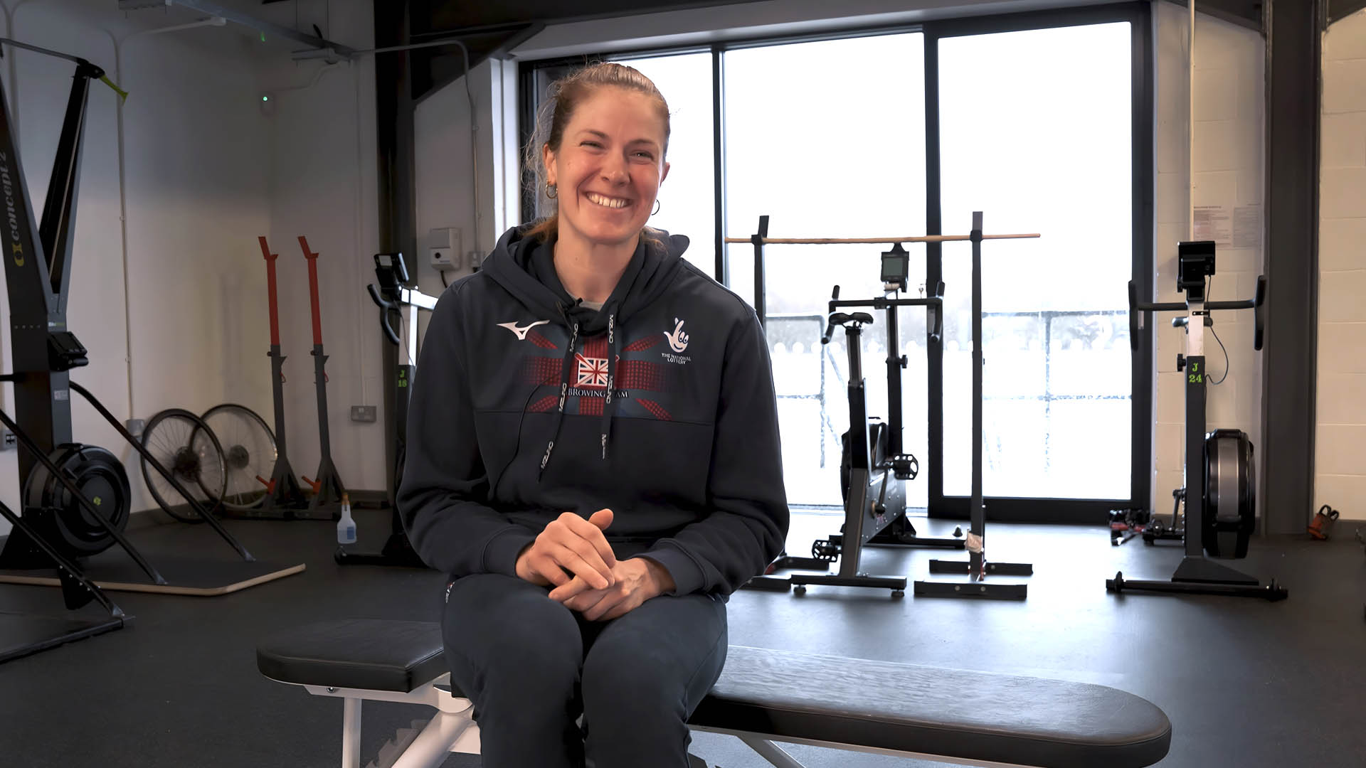 Georgie Brayshaw in British Rowing gear, talking about her passion for indoor rowing in the training center.