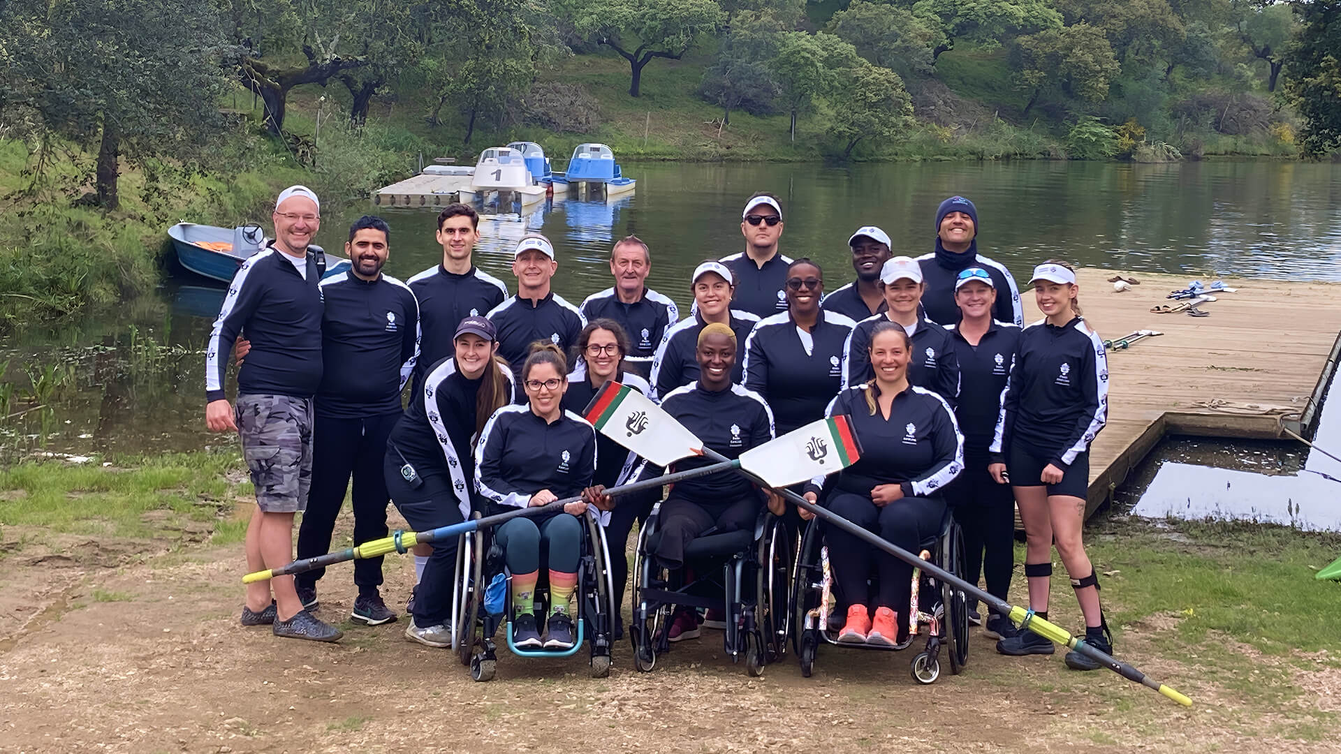 A group of para athletes and Para Rowing Foundation members posing as a group in front of a waterfront. 