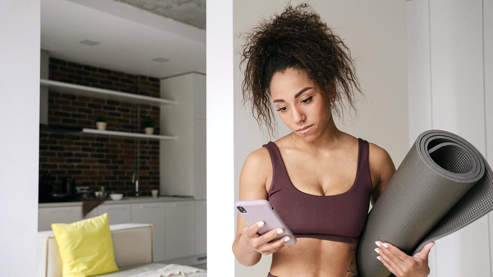 Woman in sports clothes at home with yoga mat checking mobile phone.