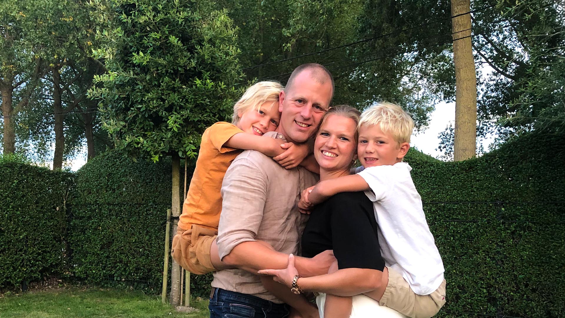 Man hugging his wife in the garden while they carry their two sons.