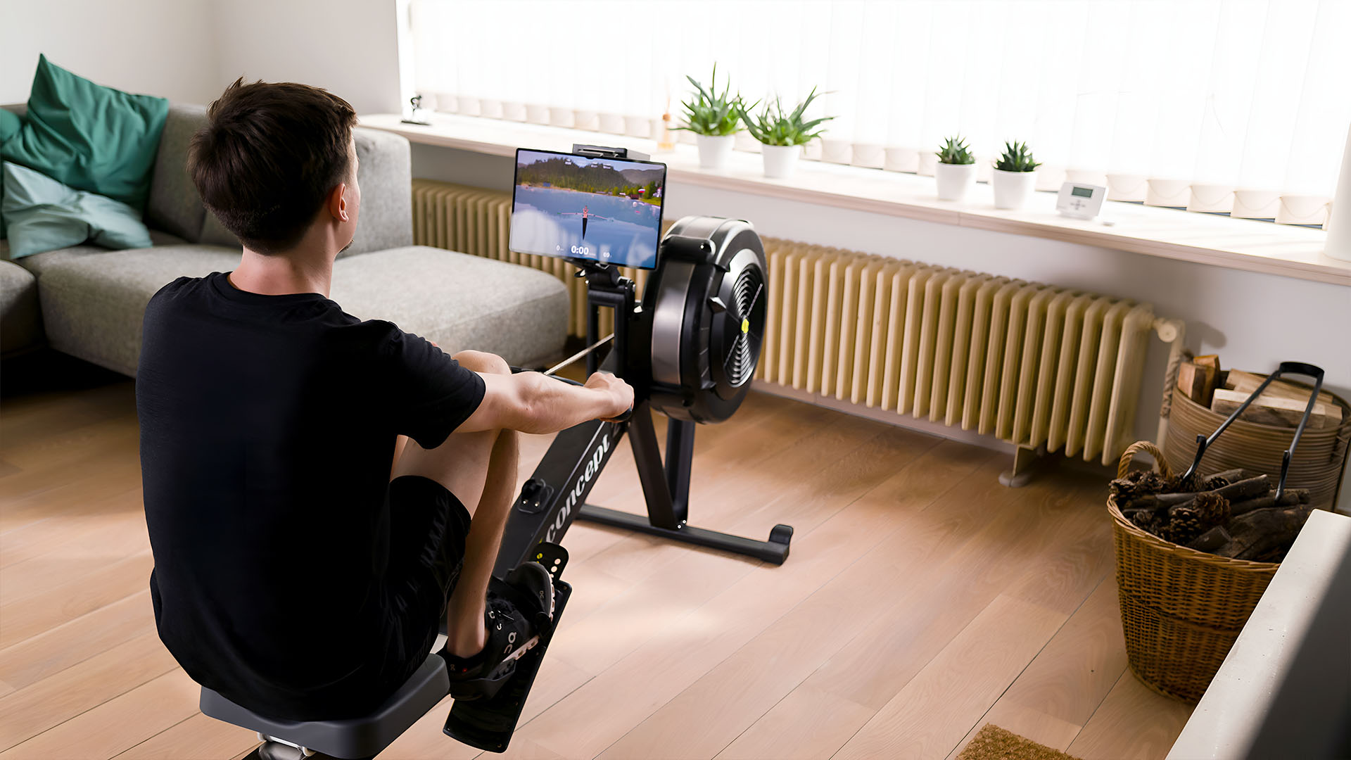 Young man rowing on Concept2 rowing machine at home on hardwood floor with EXR.