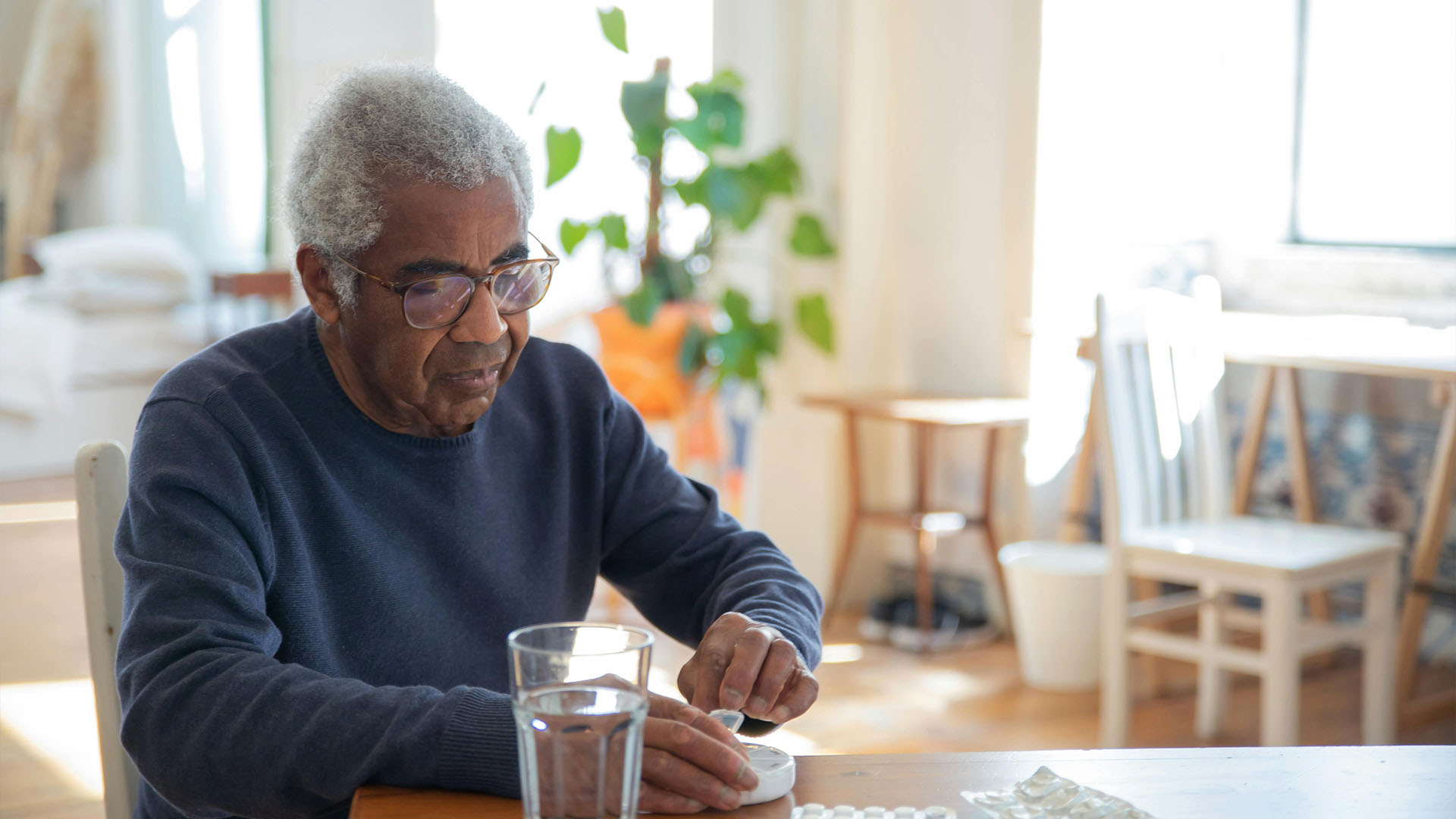 Elderly man taking his medication at a table with a glass of water.