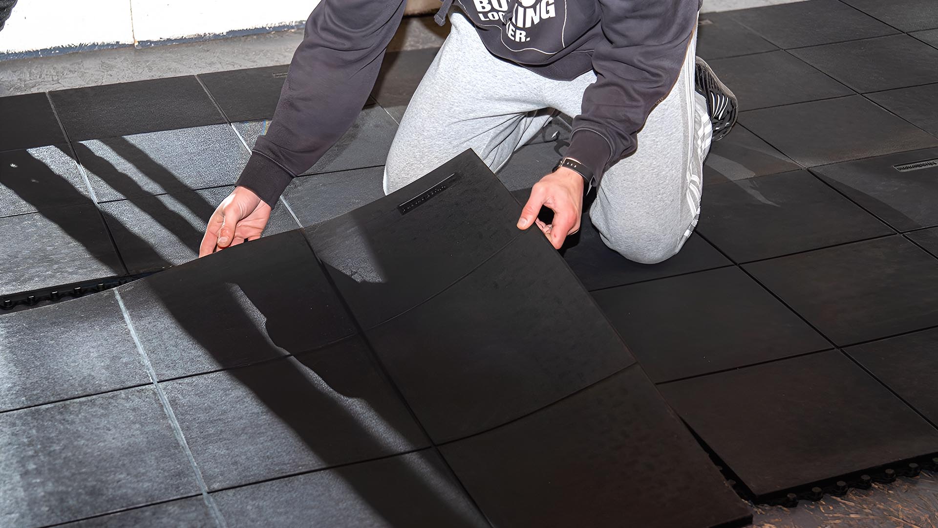 Man installing floor mat in home gym for rowing machine.