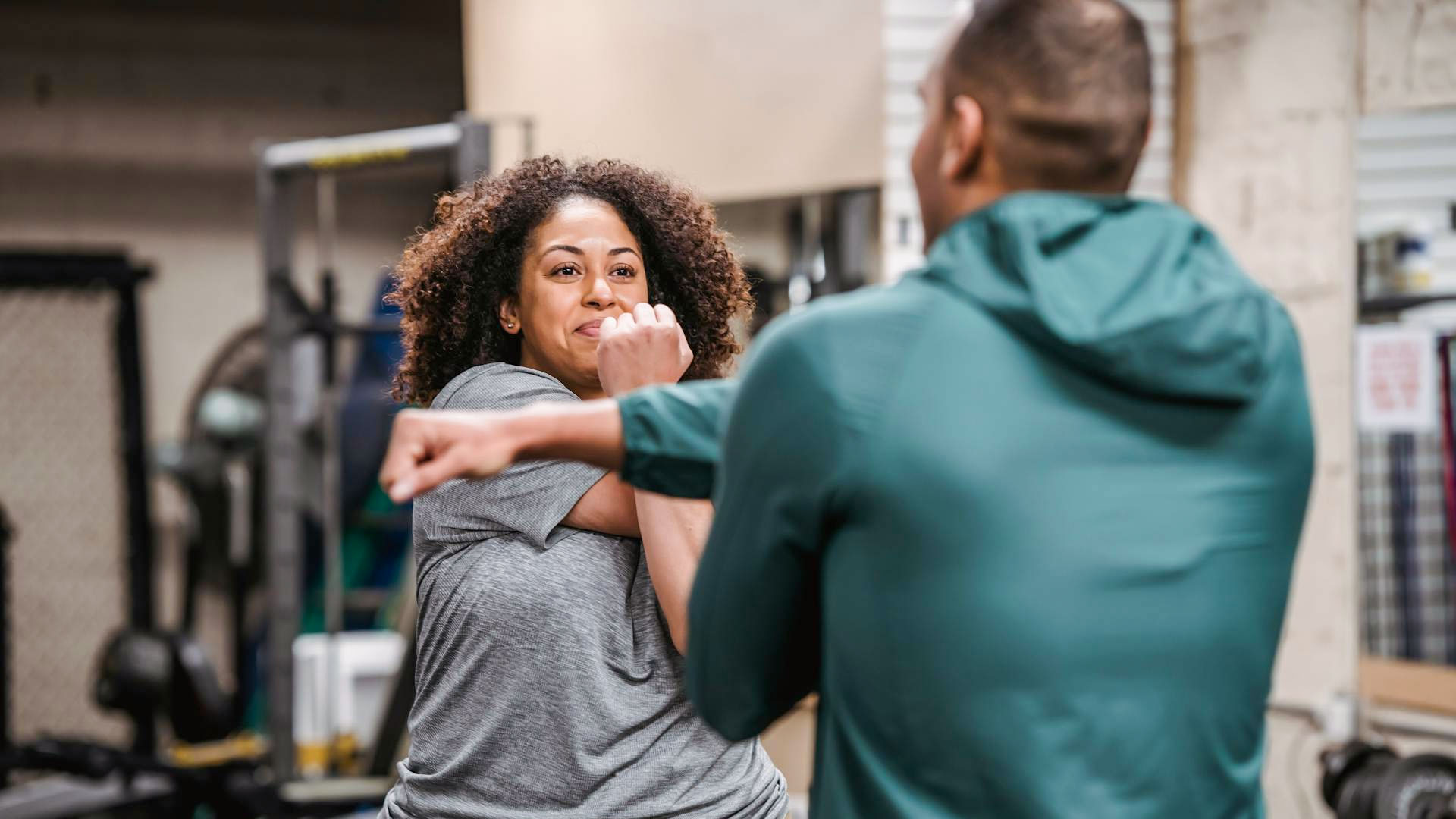 Woman in sports clothes streching with a man in workout gear at a home gym.