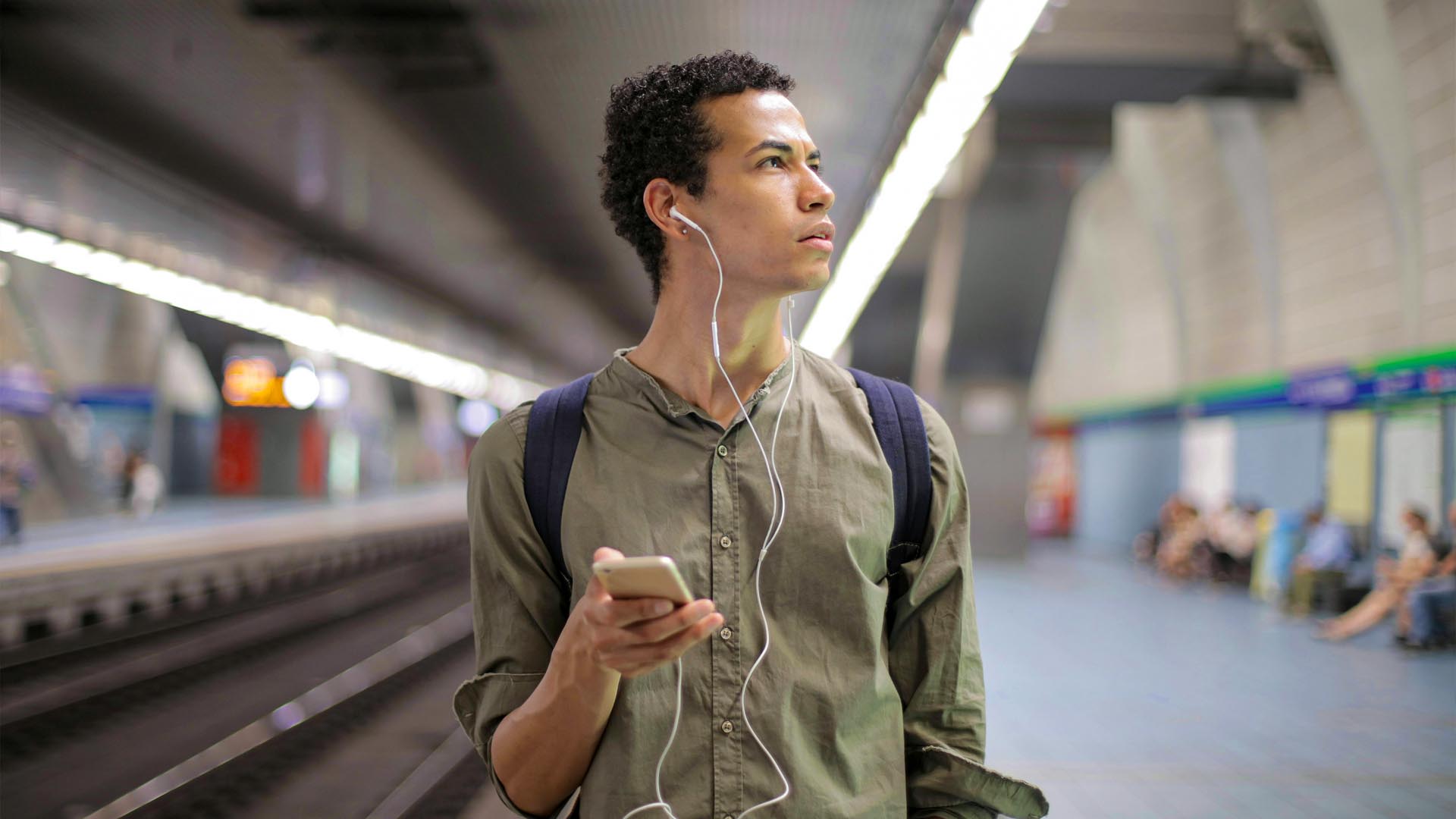 Man listening to music looking distressed by the busy environment of a metro station.