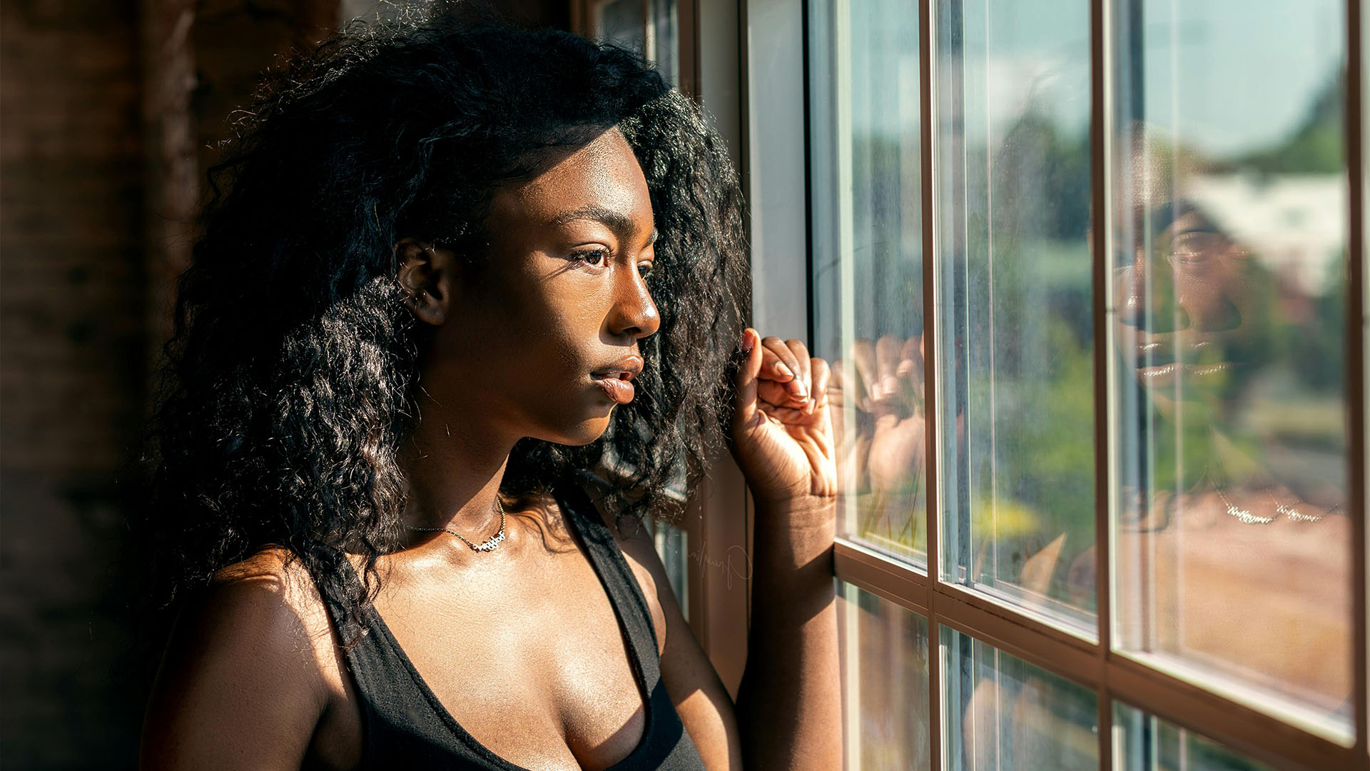Woman in sports bra standing in the sunshine next to a window.